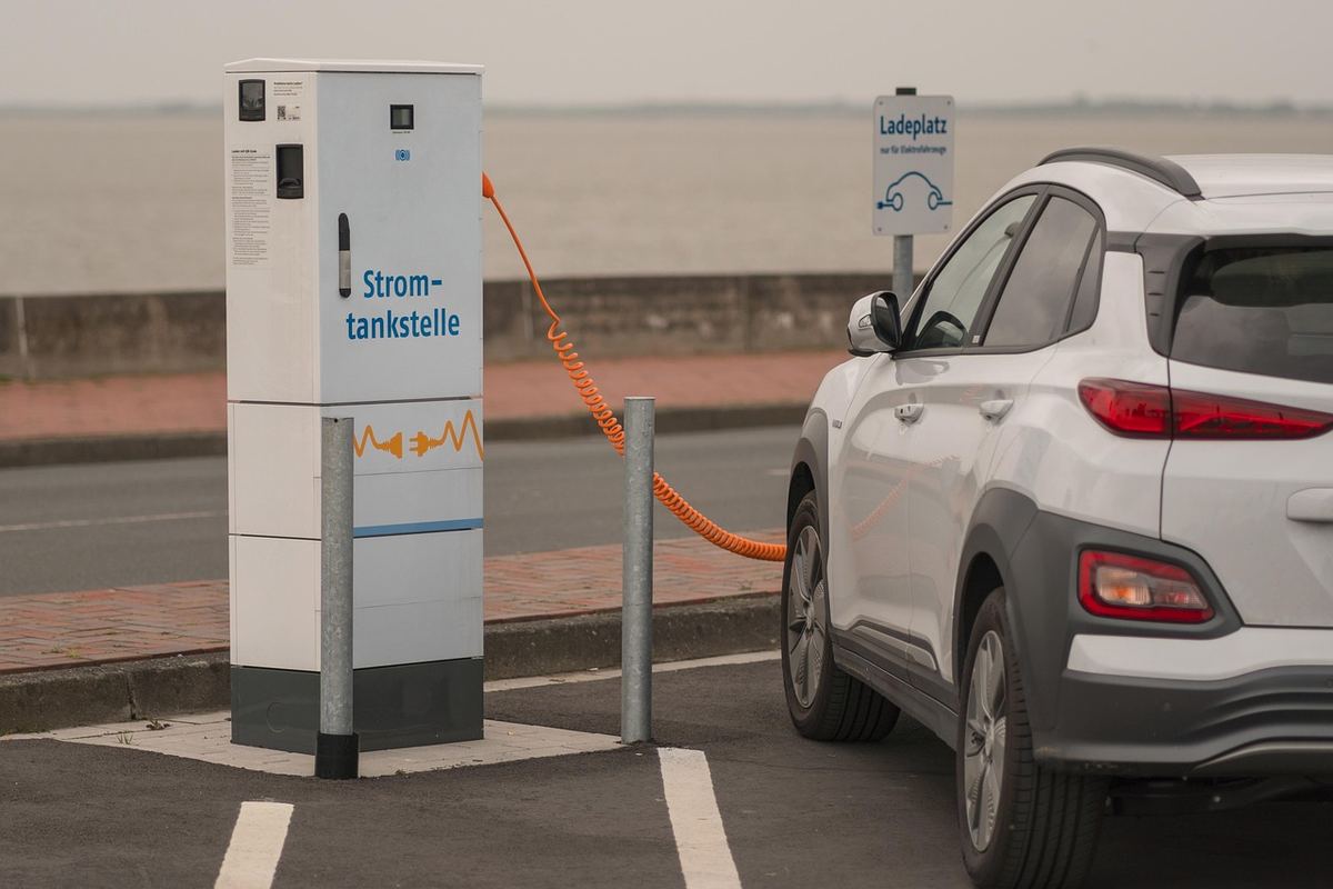 Voiture électrique blanche connectée à une borne de recharge publique en parking Voiture électrique blanche connectée à une borne de recharge publique en parking