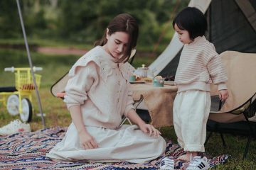 Deux enfants jouent sur un tapis à proximité d'une tente de camping beige en plein air
