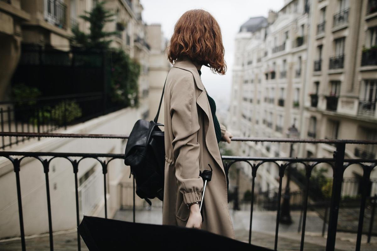 Une femme au parapluie et sac, regarde la ville depuis un balcon Une femme au parapluie et sac, regarde la ville depuis un balcon