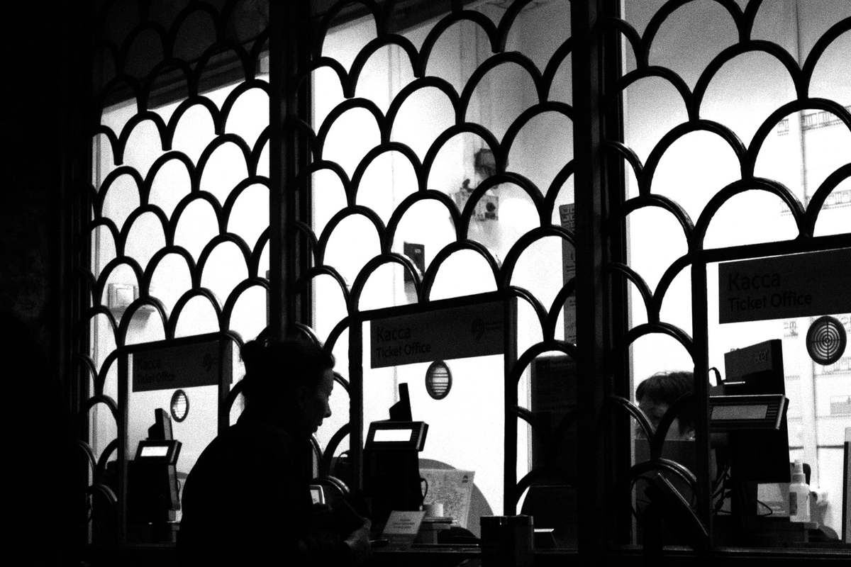 Silhouette d'une personne devant une borne informatique, à travers une fenêtre avec motifs en arc Silhouette d'une personne devant une borne informatique, à travers une fenêtre avec motifs en arc